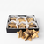 A black gift box containing star-shaped cookies in white paper cups, with three star-shaped cookies placed in front on a clean white background.