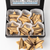 An open black gift box containing star-shaped Austrian shortbread cookies with chocolate drizzle, displayed on a white background with three cookies placed in front. 