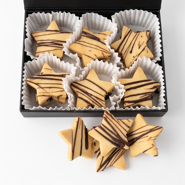 An open black gift box containing star-shaped Austrian shortbread cookies with chocolate drizzle, displayed on a white background with three cookies placed in front. 
