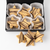 An open black gift box containing star-shaped Austrian shortbread cookies with chocolate drizzle, displayed on a white background with three cookies placed in front. 