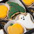 A close-up of Halloween-themed iced cookies in a black box including a green witches's hat cookie with red dots, a white ghost cookie, and yellow pumpkin cookie.