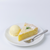 A slice of lemon tart dusted with powdered sugar, served with a scoop of vanilla ice cream and a silver fork on a white plate against a clean white background.