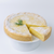 A lemon tart with a slice cut out and a piece pulled forward, sitting on a white pedestal plate. The tart is dusted with powdered sugar and garnished with a small green rosemary sprig, photographed against a clean white background.