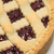 A close-up of a baked Linzer Tart with a lattice crust and raspberry filling, photographed on a white plate.