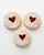 Three heart-shaped cookie sandwiches with red jam filling on a white background