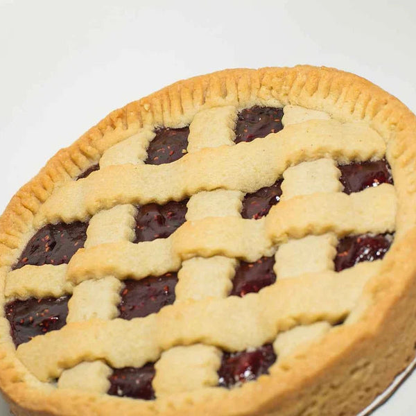 A close-up of a freshly baked lattice-topped Linzer Tart Cake with golden-brown crust and raspberry filling, photographed on a clean white background.