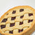 A close-up of a freshly baked lattice-topped Linzer Tart Cake with golden-brown crust and raspberry filling, photographed on a clean white background.