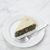 A slice of poppy seed cake, served on a white plate with a silver fork on a white marble surface.
