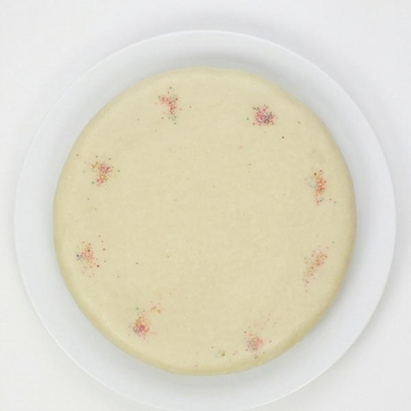 A poppy seed cake with a marzipan topping with small scattered red and green sprinkles, presented on a white plate against a clean white background.