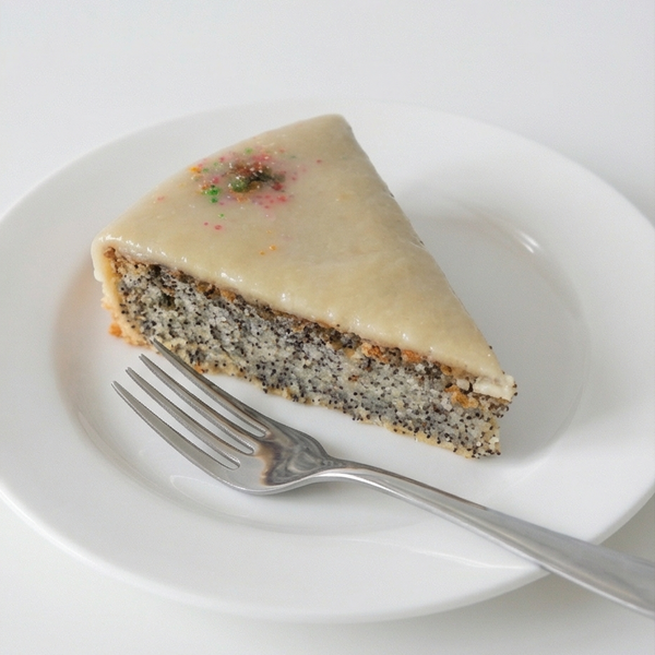 Slice of poppy cake with marzipan topping on a white plate with a fork