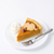 A slice of pumpkin pie on a white plate with a dollop of whipped cream and a small cranberry garnish, accompanied by a silver fork on a clean white background.