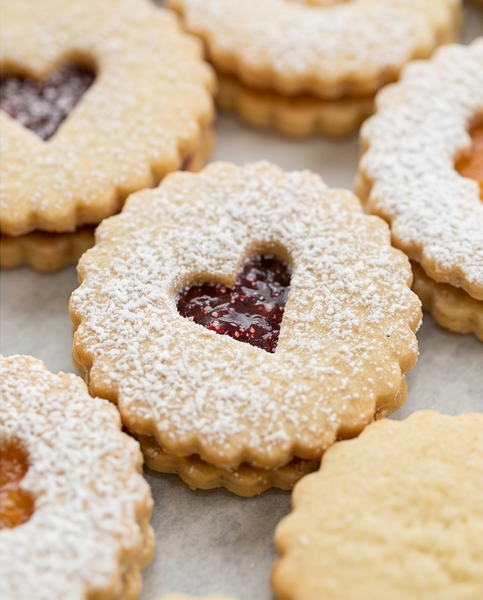 Linzer cookies with heart-shaped cutouts filled with jam on a marble surface