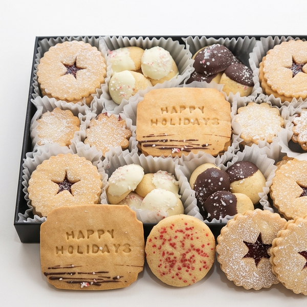 A gift box of assorted holiday cookies on a white background, including star-shaped linzer cookies, chocolate-dipped cookies, and cookies embossed with 'HAPPY HOLIDAYS'.
